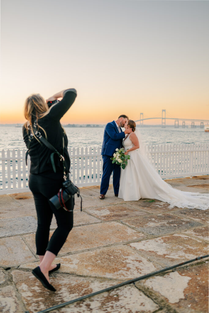 Wedding Photographer Stacey Lillian Photography taking a picture of newlyweds in front of the Newport Bridge